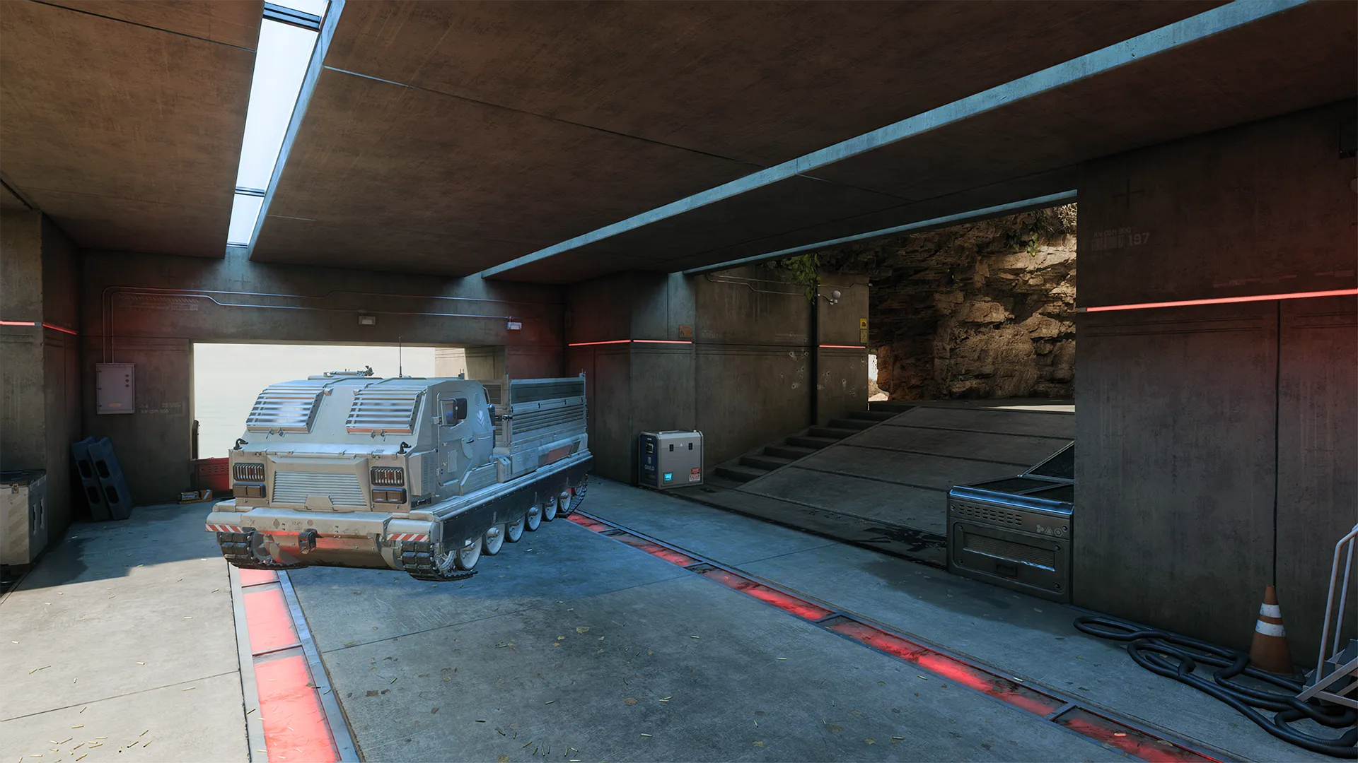 A military garage with a white armored vehicle parked on a concrete floor beneath a low ceiling. Red lighting strip lighting and skylights provide illumination, and the garage opens to a rocky cliffside environment.