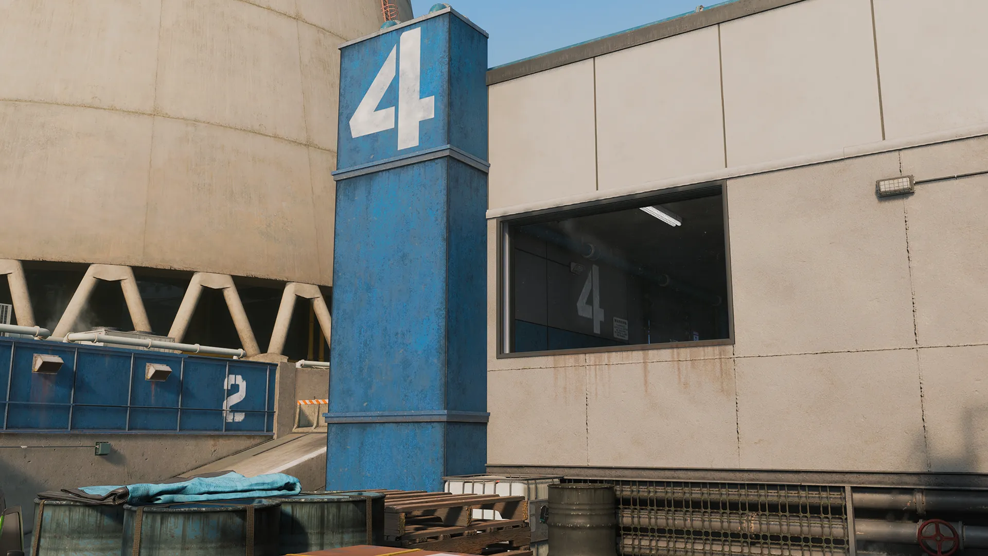 An exterior industrial building features a tall blue pillar marked with a large white number “4,” flanked by metal walls, vents, and stacked pallets. The scene suggests a numbered facility zone with functional, weathered surfaces under clear daylight.