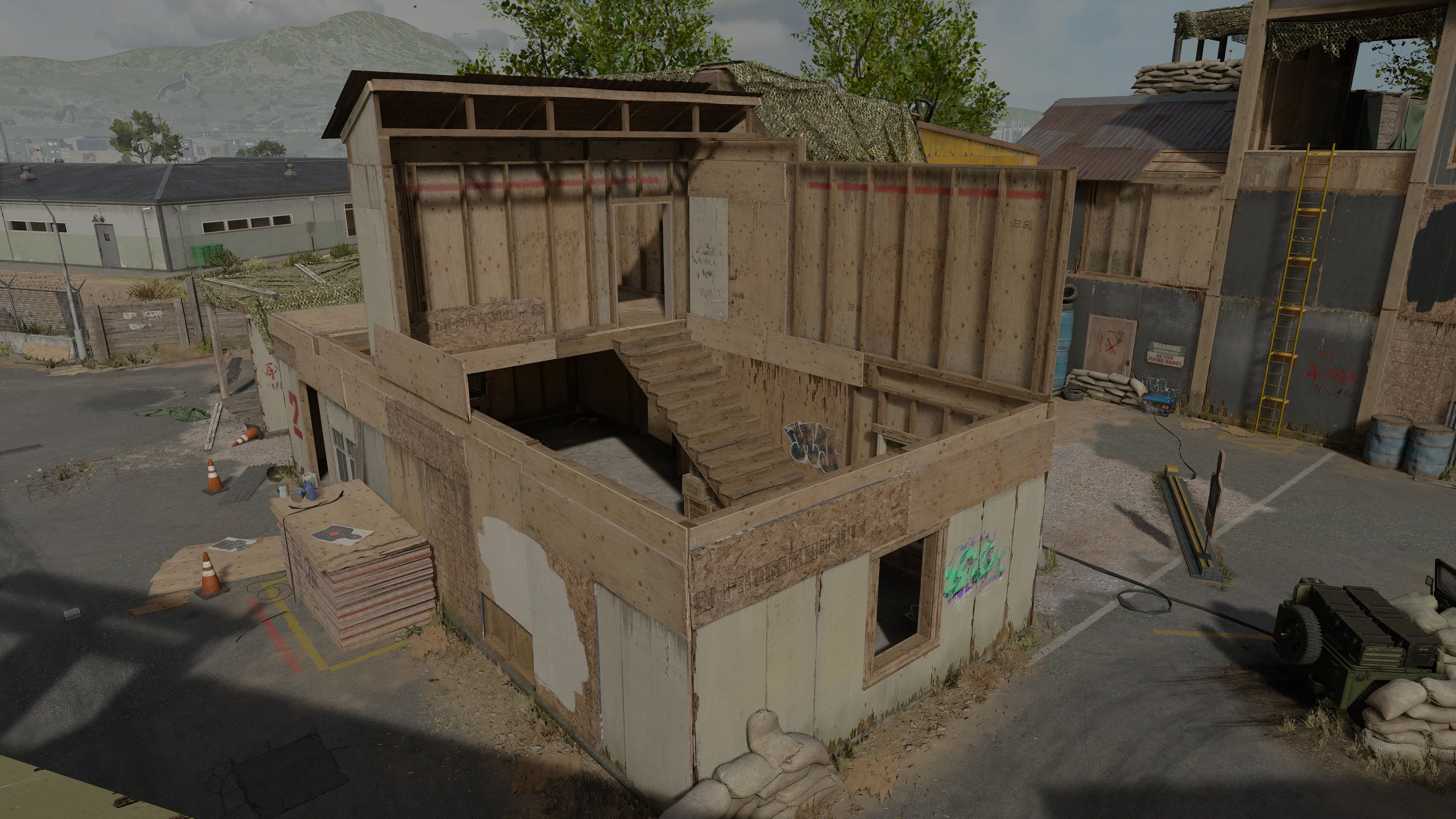 A two-story wooden training building with exterior stairs and open windows inside a military firing range compound.