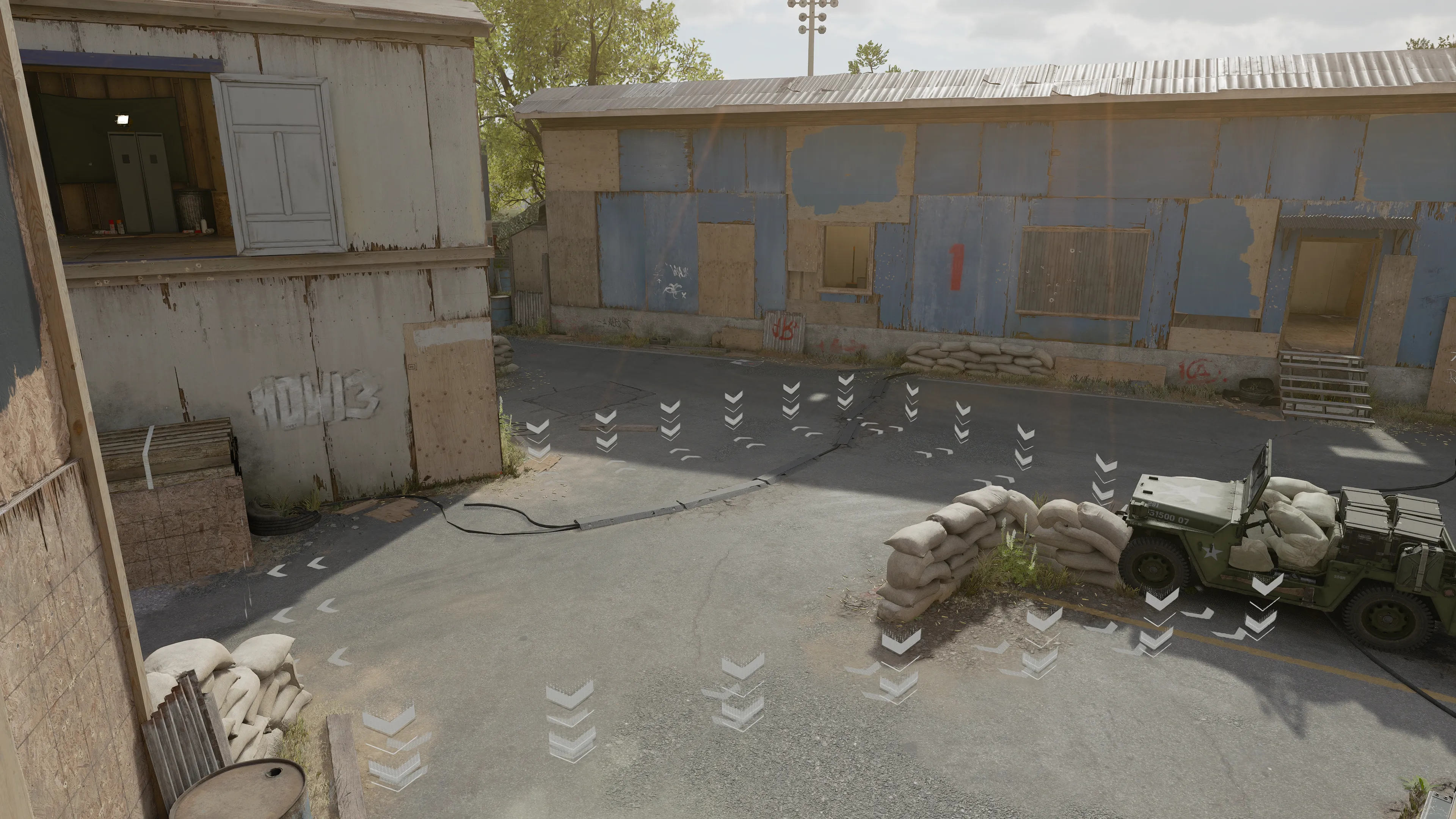 A paved intersection in the training yard with sandbag cover and a parked military jeep beside weathered wooden buildings.