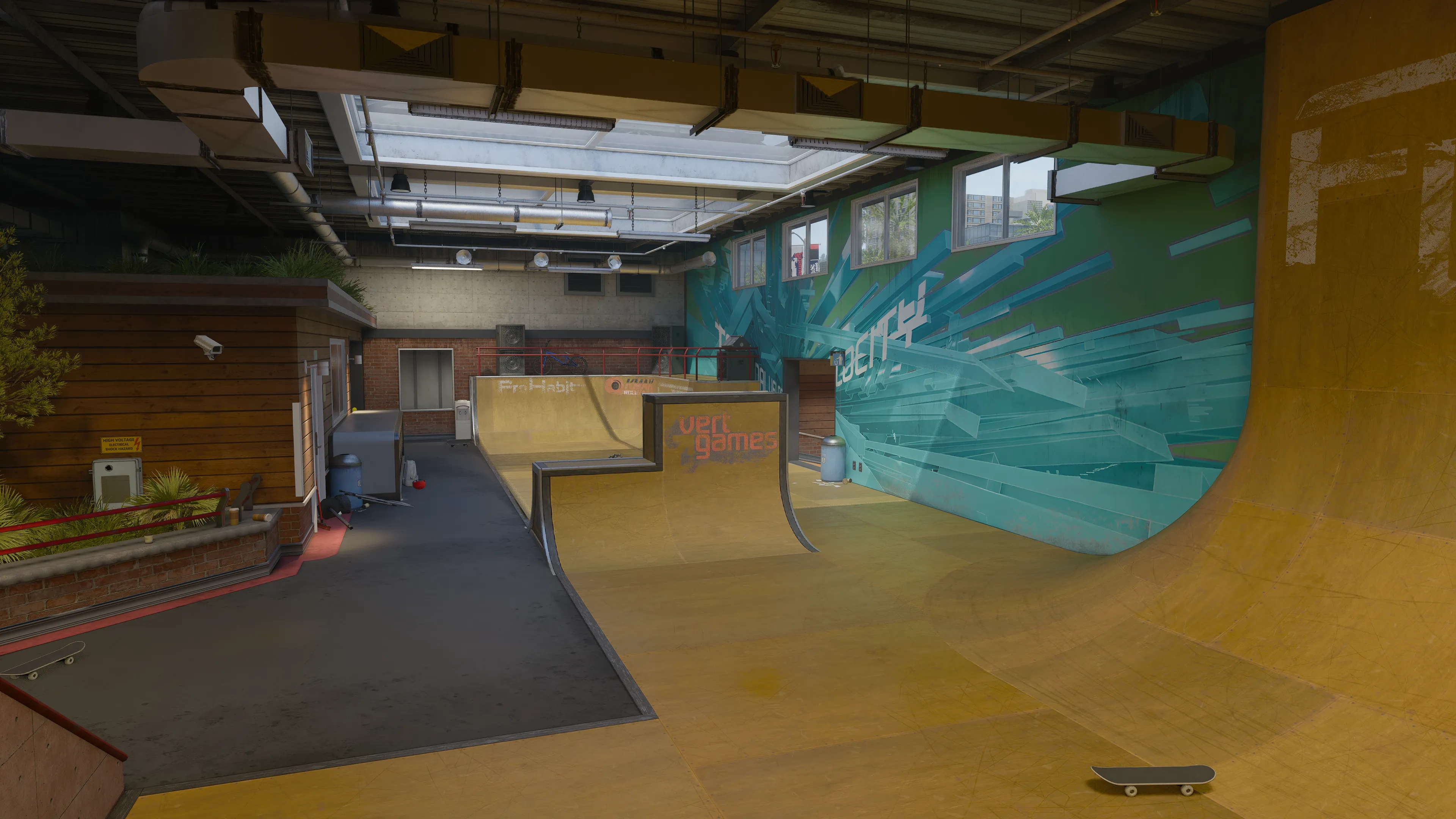 An indoor skate facility with wooden ramps, graffiti-style wall art, skylights overhead, and scattered skateboards on the floor.