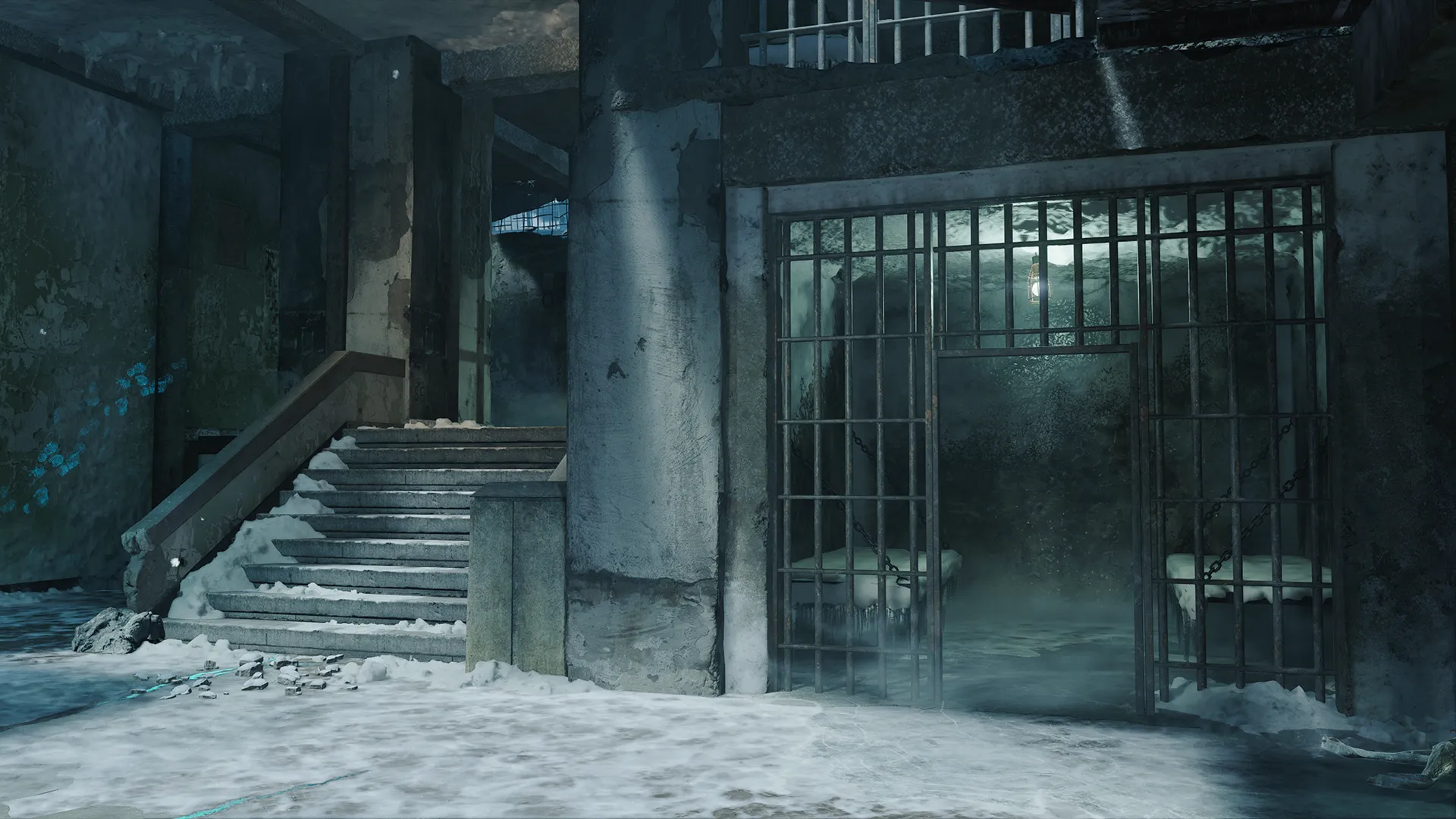A cold, abandoned prison-like interior with barred cells, concrete pillars, drifting mist, and patches of snow, illuminated by faint blue light that emphasizes the harsh, frozen environment.