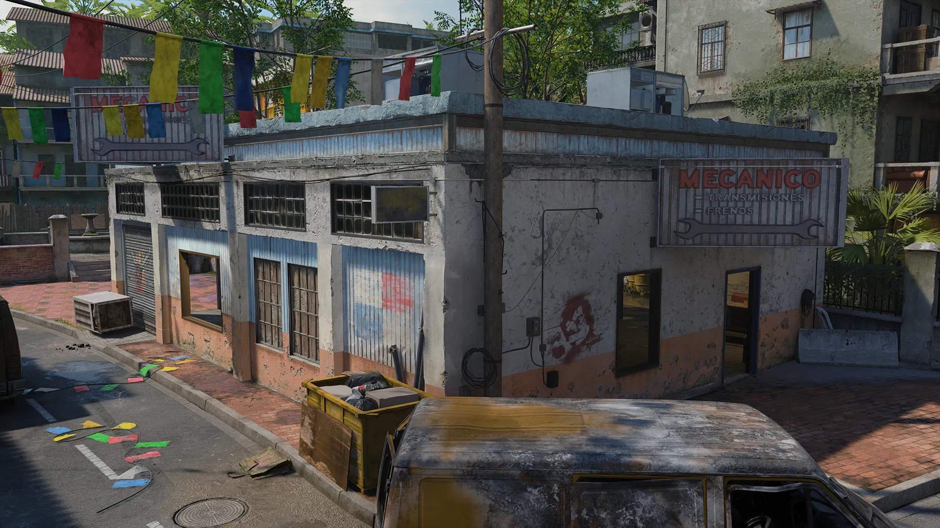 Street corner with a small auto repair building, hanging banners, and damaged vehicles.