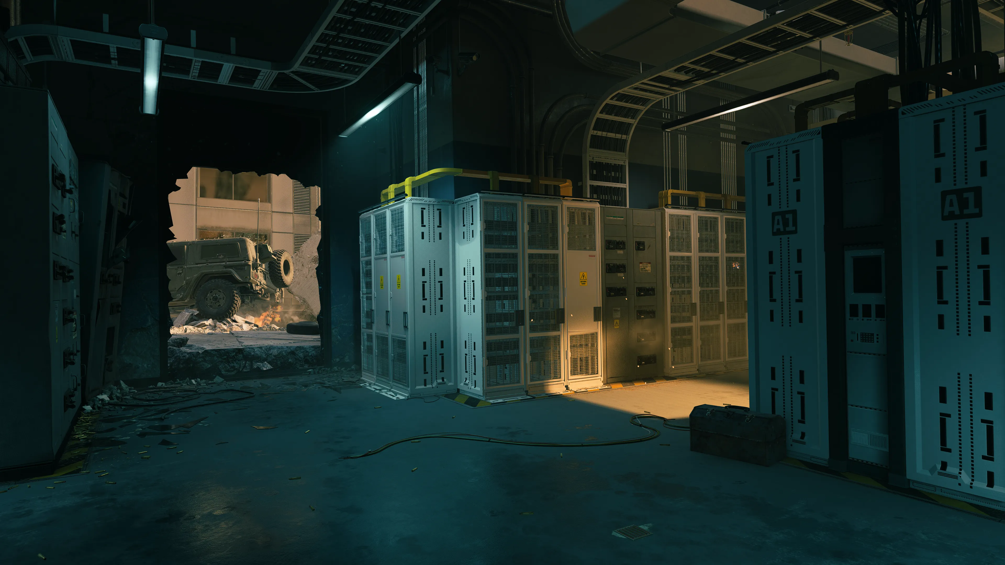 A server room filled with tall electrical cabinets and cables, with a large hole blown through the wall revealing a military vehicle outside on a destroyed freeway.