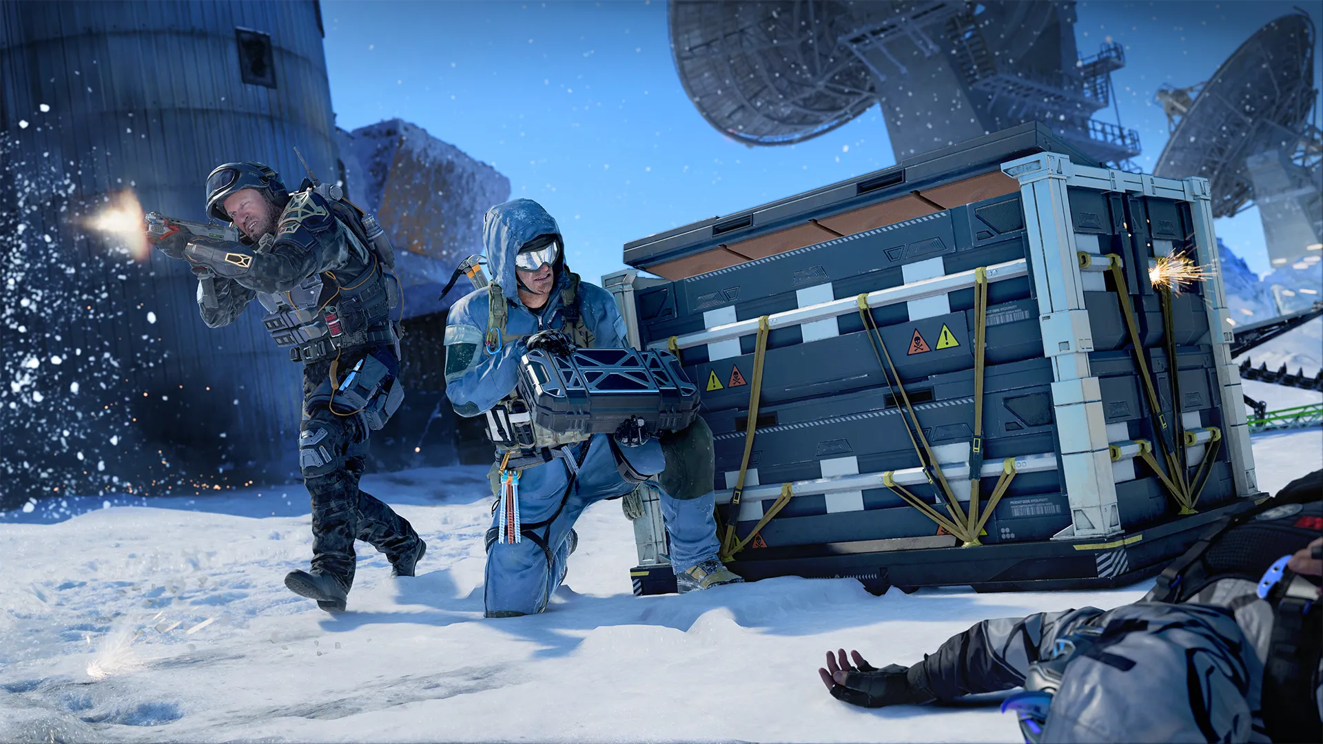 Two soldiers take cover behind a crate in the snow, one firing while the other handles a device.