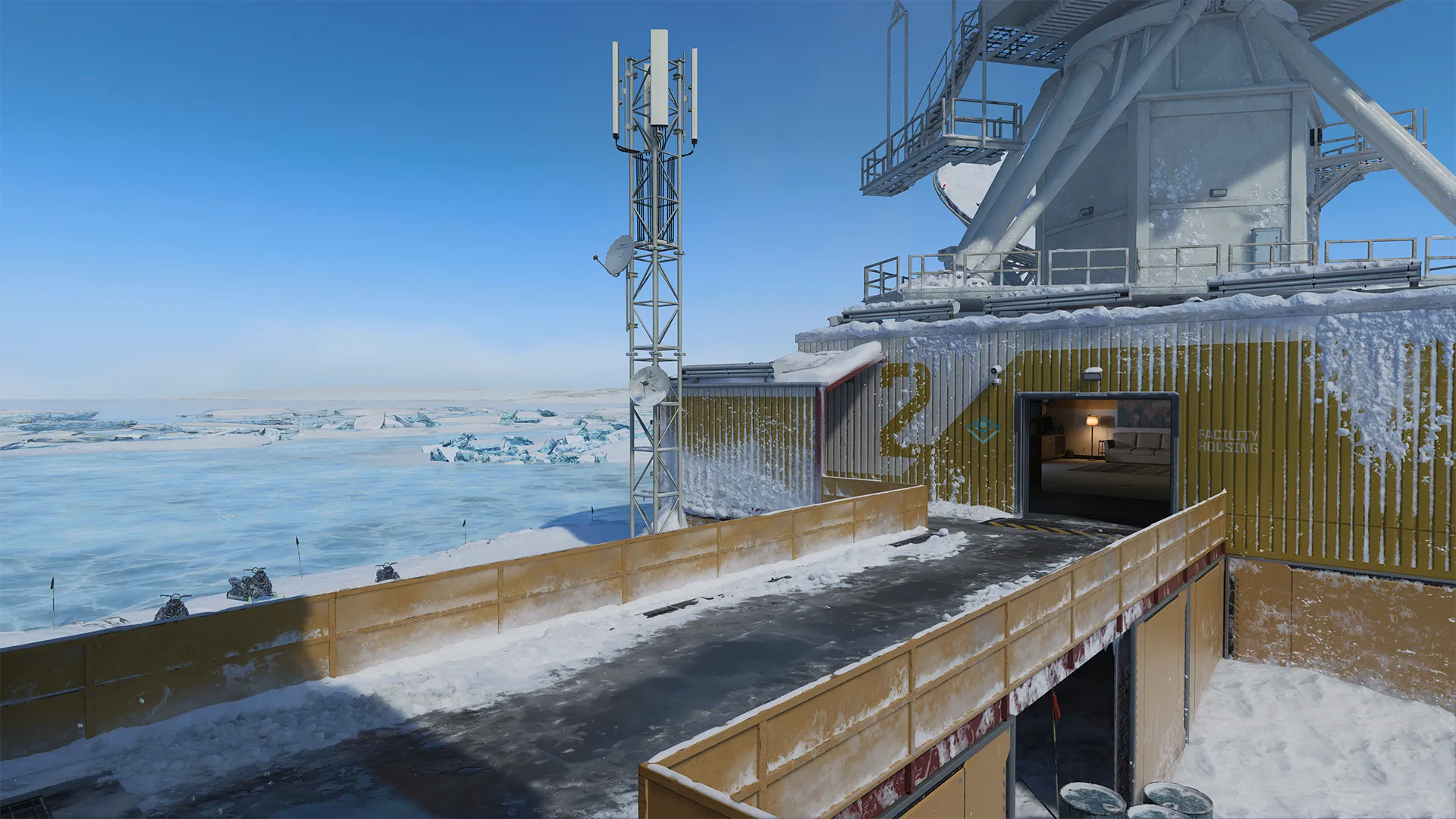 Snowy research station with a raised walkway leading into a building marked “2” beside icy water and antennas.
