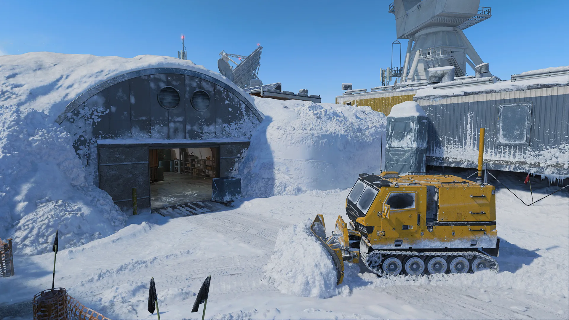 Yellow tracked snow vehicle plows snow outside a rounded bunker entrance buried in drifts.